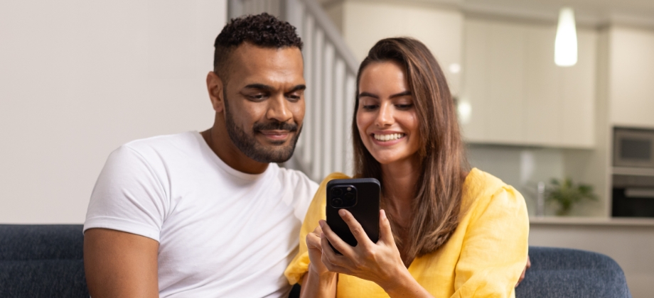 Man and woman sitting on couch looking at phone smiling